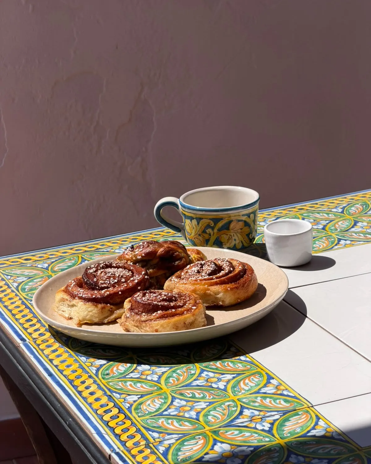 Un piatto di girelle e una tazzina di caffè su un tavolo di maioliche, in terrazza al sole
